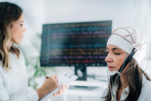 Devojka sa EEG priključcima na glavi sedi dok doktorka na monitoru prati njene moždane talase